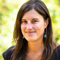 Person smiling in front of green background outside.