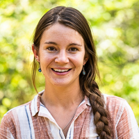 Person smiling in front of green background outside.