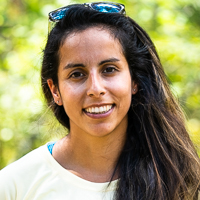 Person smiling in front of green background outside.