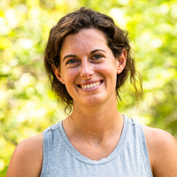 Person smiling in front of green background outside.