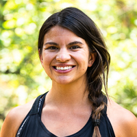 Person smiling in front of green background outside.
