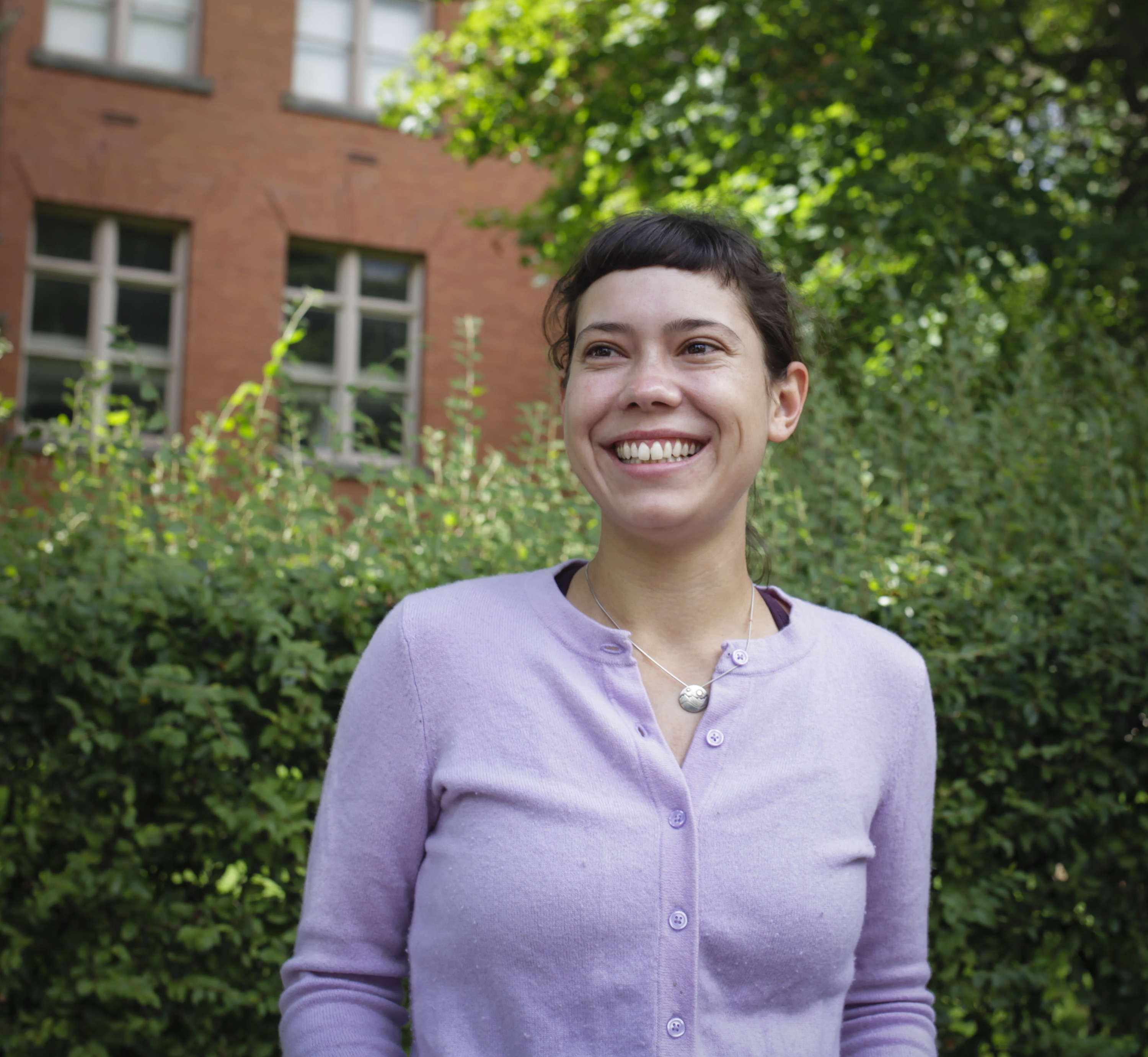 Person smiling in front of green background outside.
