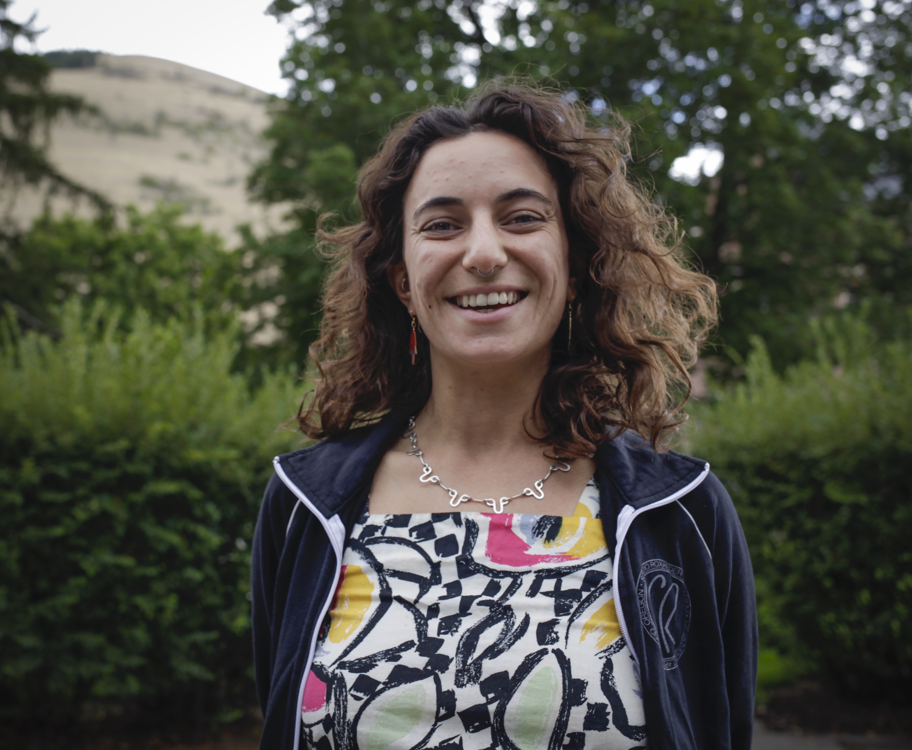 Person smiling in front of green background outside.