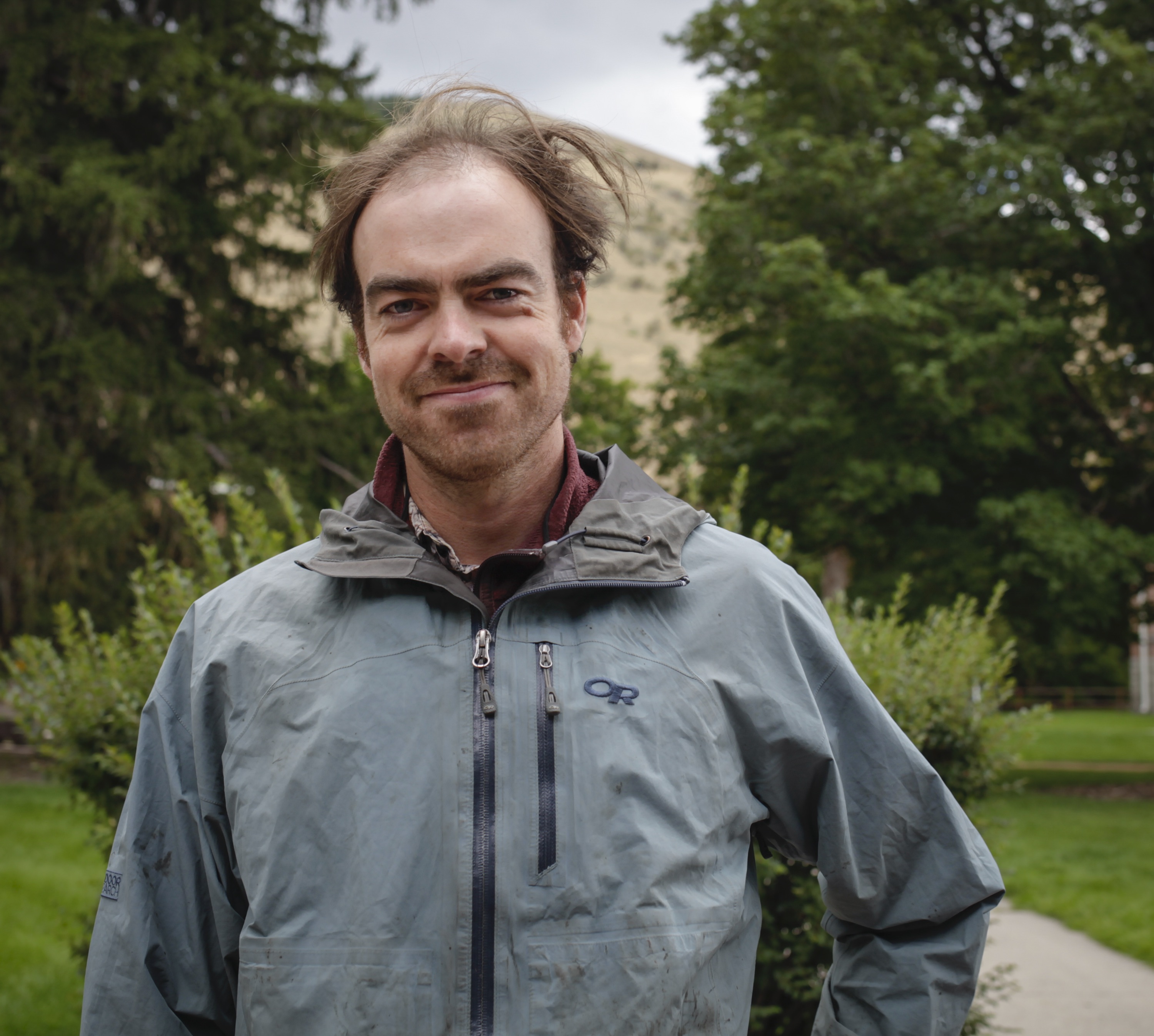 Person smiling in front of green background outside.