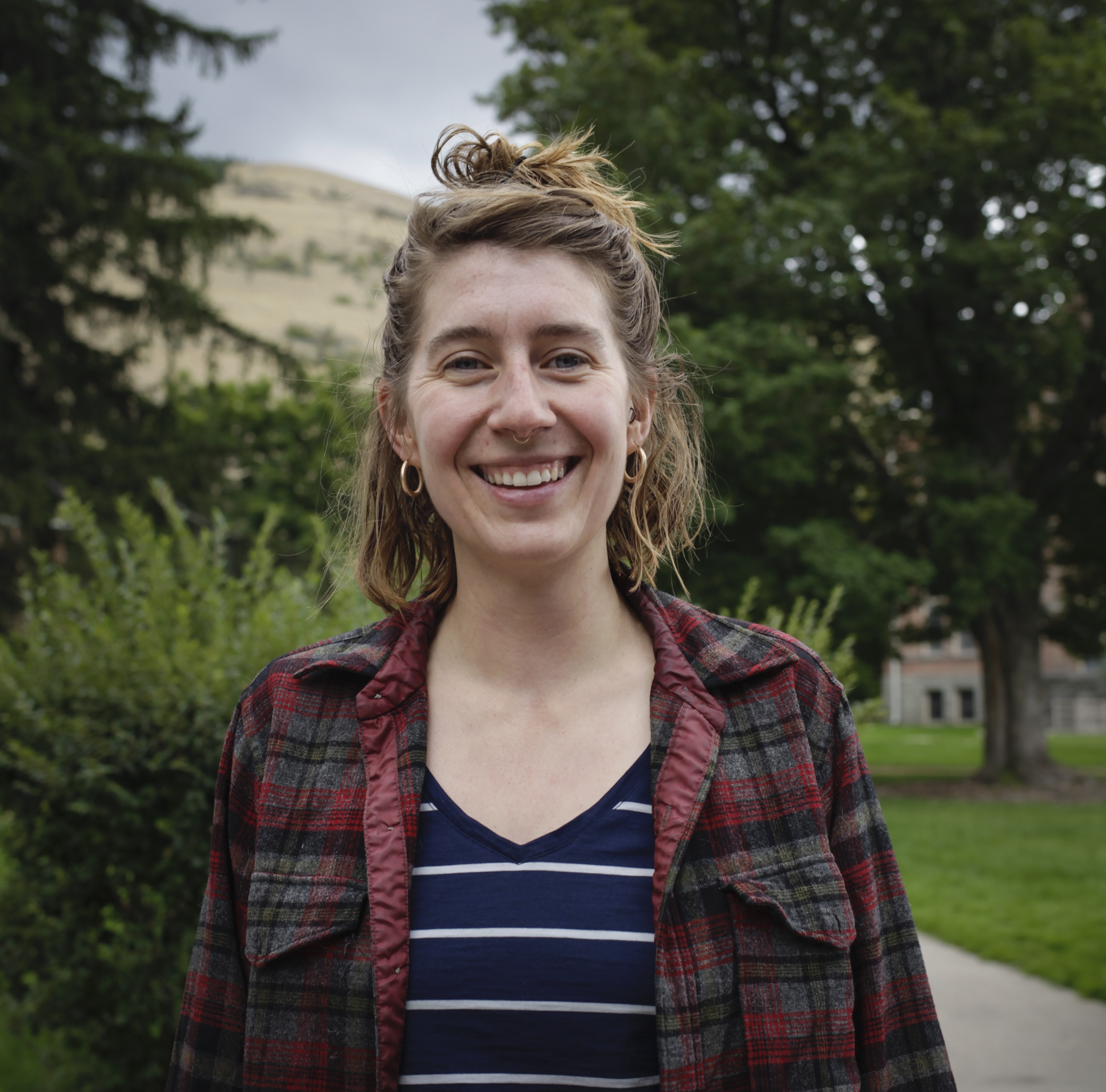 Person smiling in front of green background outside.