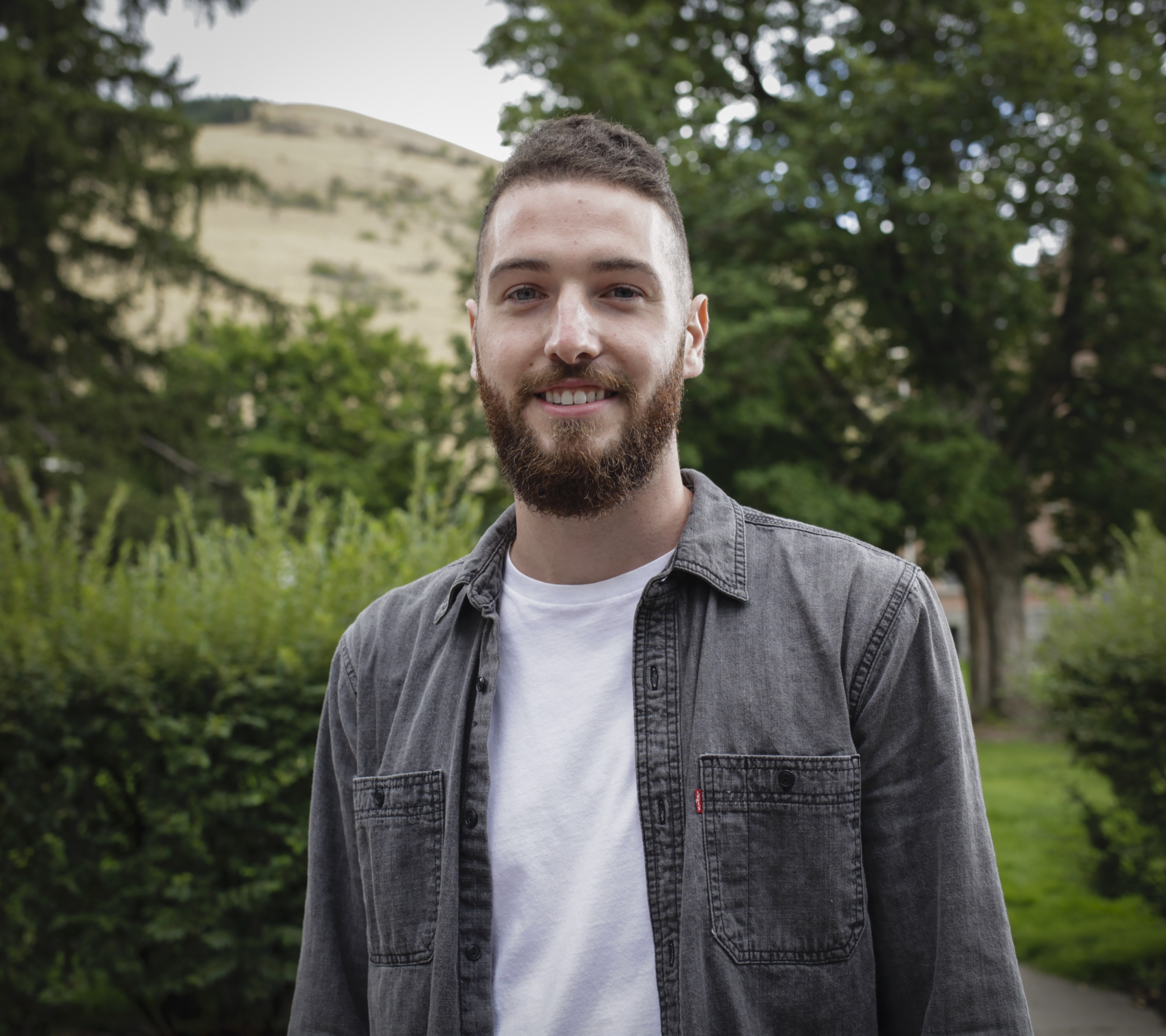 Person smiling in front of green background outside.