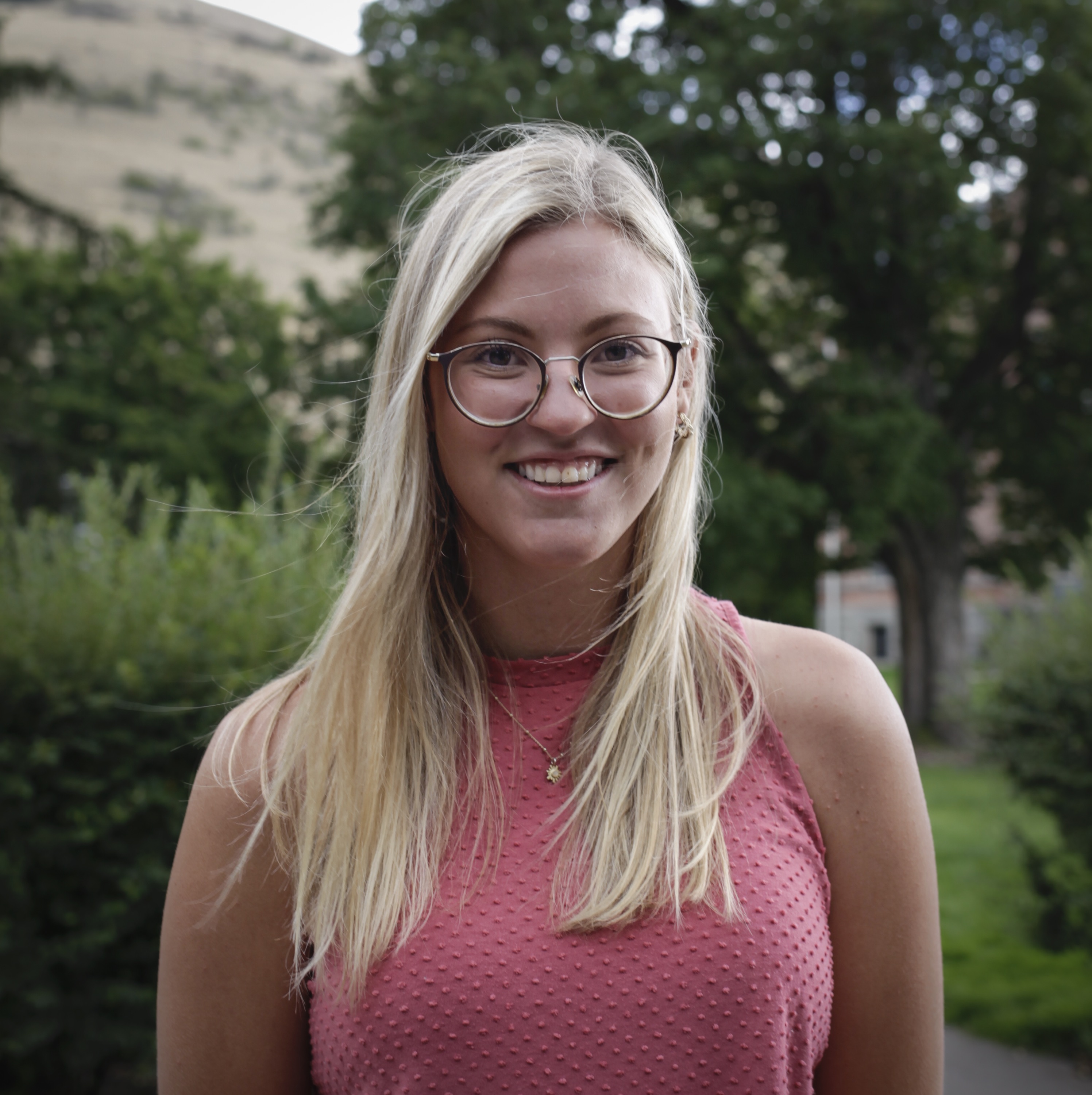 Person smiling in front of green background outside.