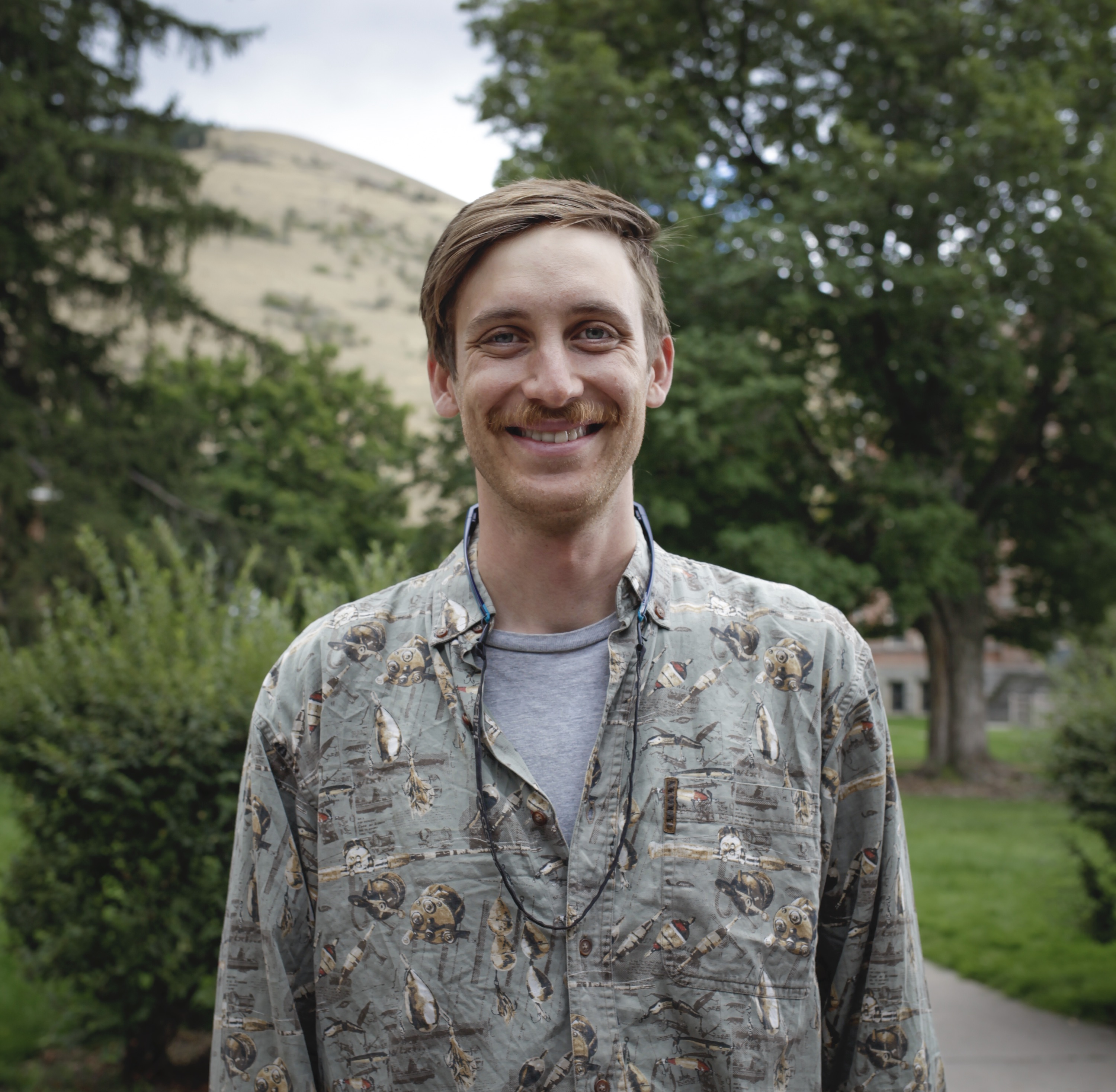 Person smiling in front of green background outside.