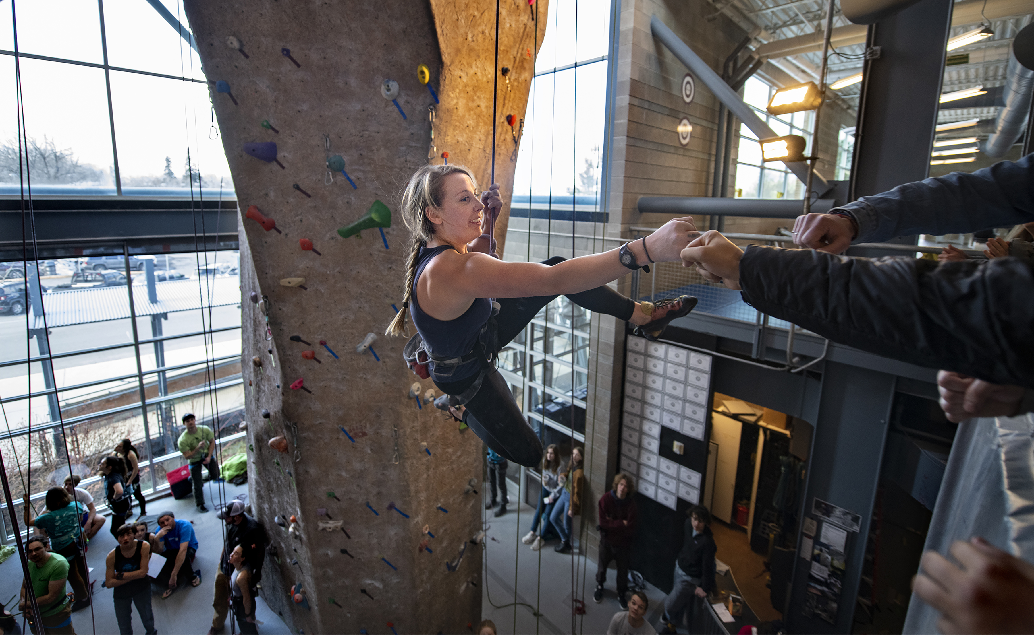 female students climbs on climbing wall in front of new lights