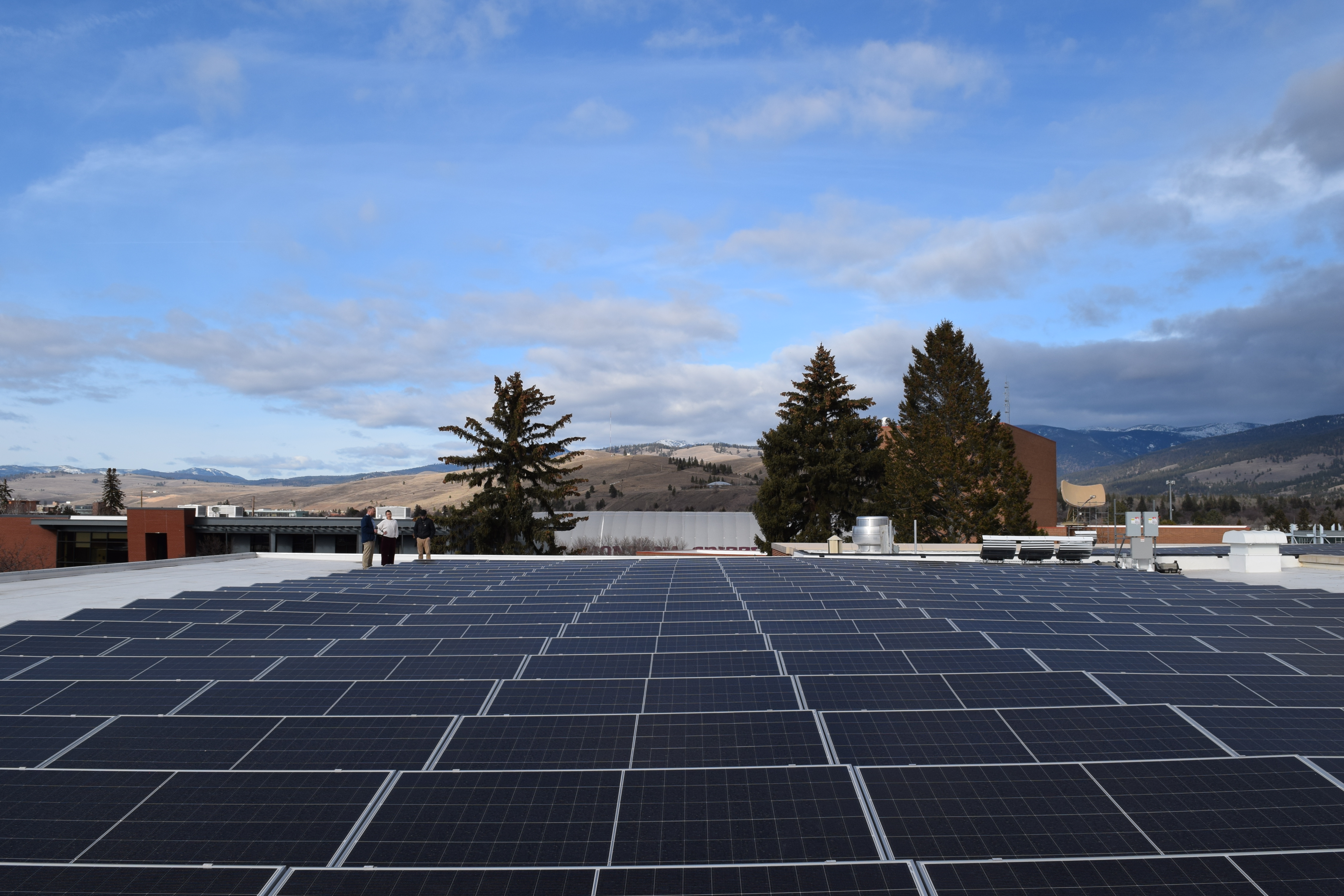 Rooftop solar panel array with mountains and a partly cloudy sky in the background.
