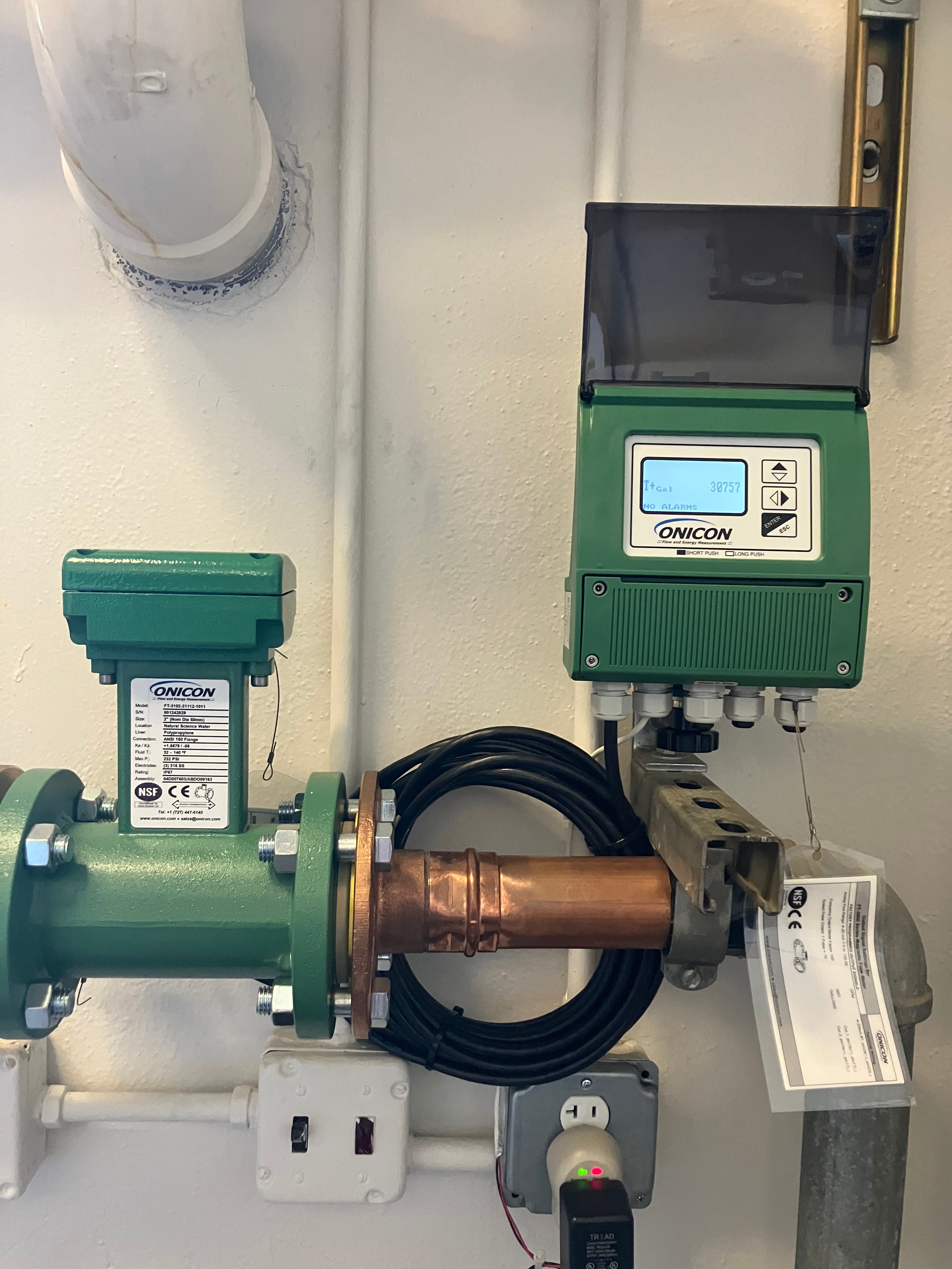 Green ONICON flow meter and electronic display mounted on a copper pipe with wiring and conduit.