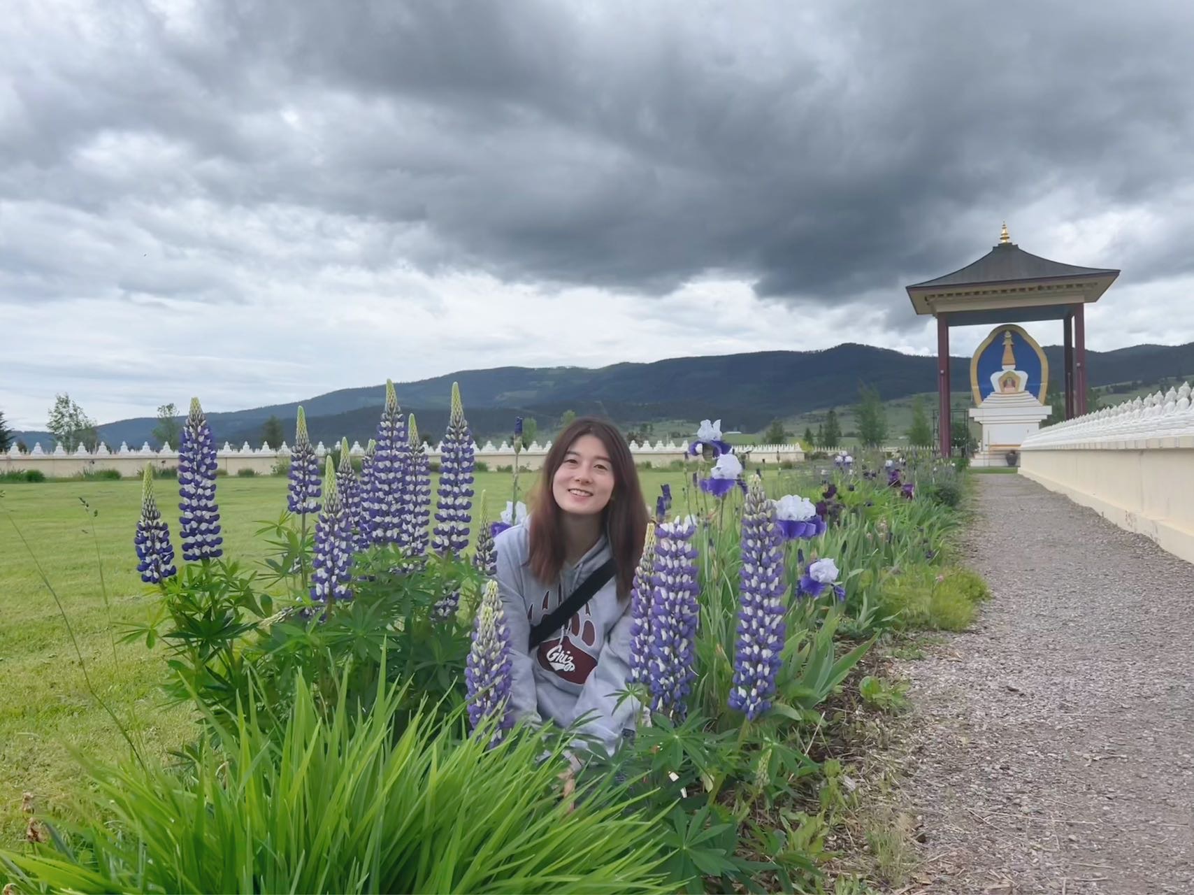 Yusi Chen is smiling in a grey UM hoodie in purple flowers with mountains in the background at the Garden of 1000 Buddahs