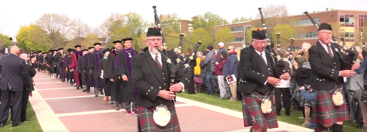 Start of graduation walk. Picture of bagpipers leading law students and faculty who are wearing robes