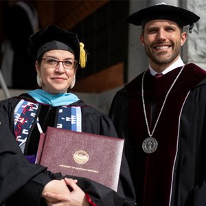 The late Bonnie Heavy Runner’s daughter, Aislinn Roux, accepts the honorary PhD from President Seth Bodnar