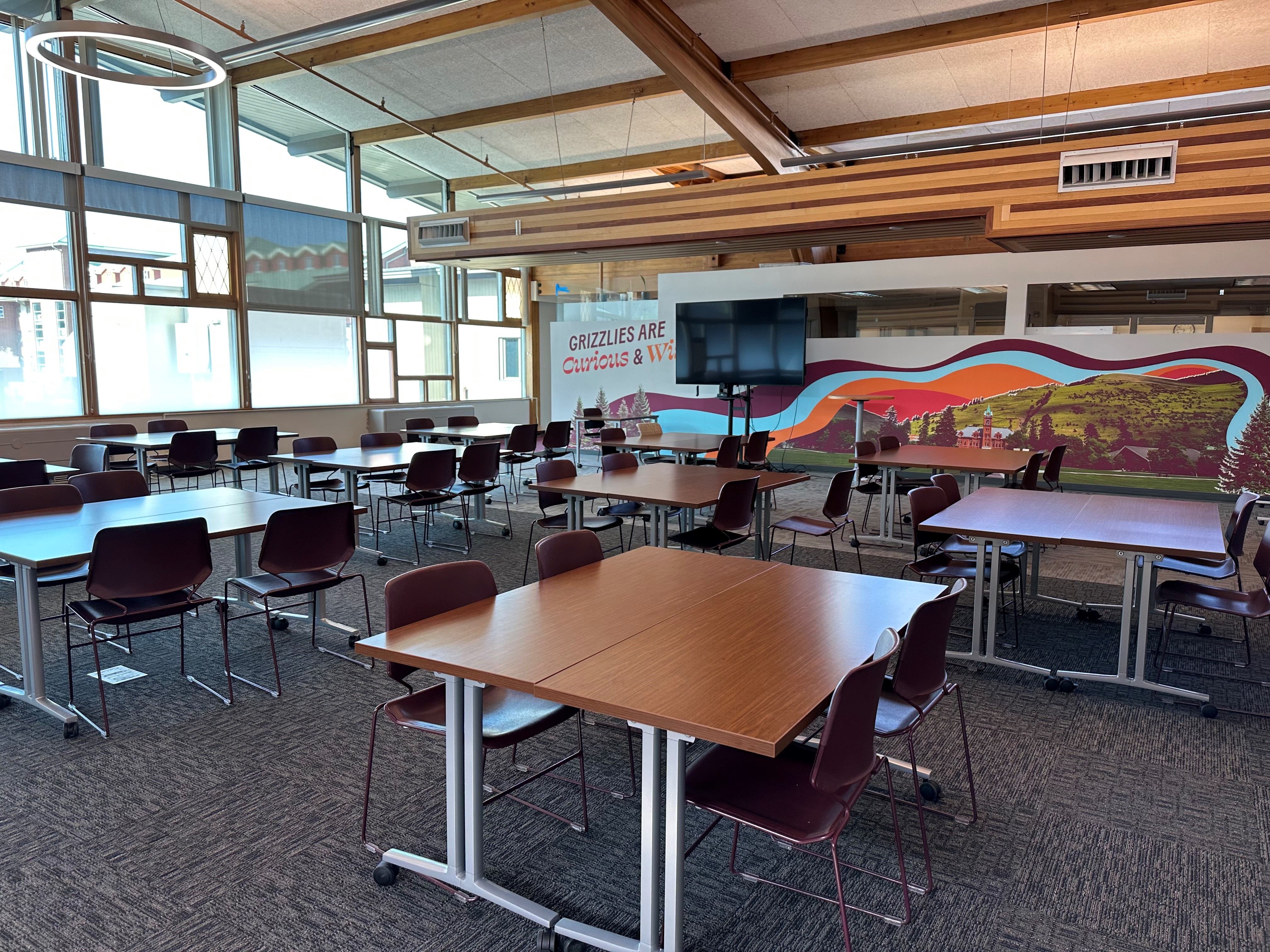 a photo of the tables and chairs that make up the employee learning space, with the large tv in the background