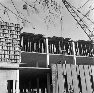 Black and white photograph of a construction site featuring a crane and workers on a building under construction.