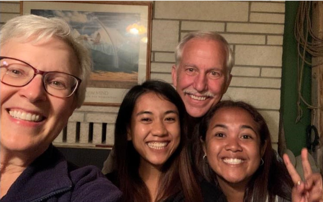 Two hosts and their two guests smiling for a selfie indoors, with one person flashing a peace sign.
