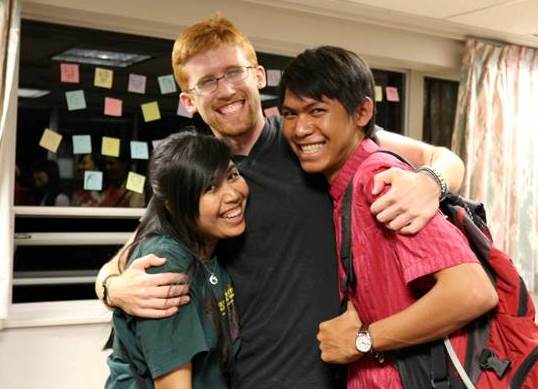 A red-headed UM student hugging two southeast Asian participants.