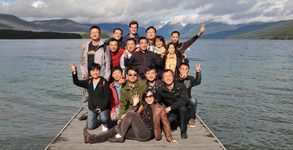 A group of male and female program participants from Southeast Asia pose on a pier over a lake with mountains in the background. 