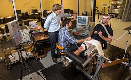 UM researcher Matt Bundle (left) works with exercise science grad students Tyler Gallo (center) and Riley Shaw on an experiment using a custom-built knee extension odometer.