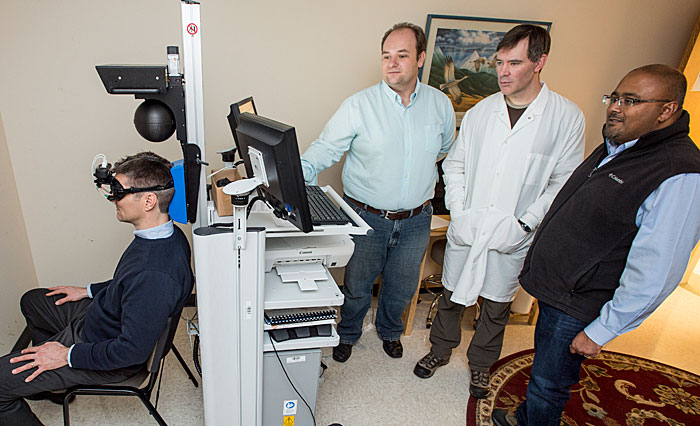 Researchers Alex Santos, Tom Rau and Sarj Patel (standing left to right) test the extent of brain injuries using equipment that tracks the eye movements of subjects.