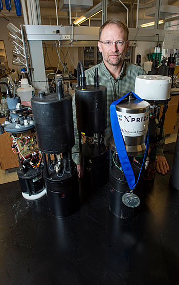 Chemistry Professor Mike DeGrandpre poses in his UM lab with several versions of the sensors he developed with Sunburst Sensors LLC, including a new titanium version that can function at 3,000 meters underwater.
