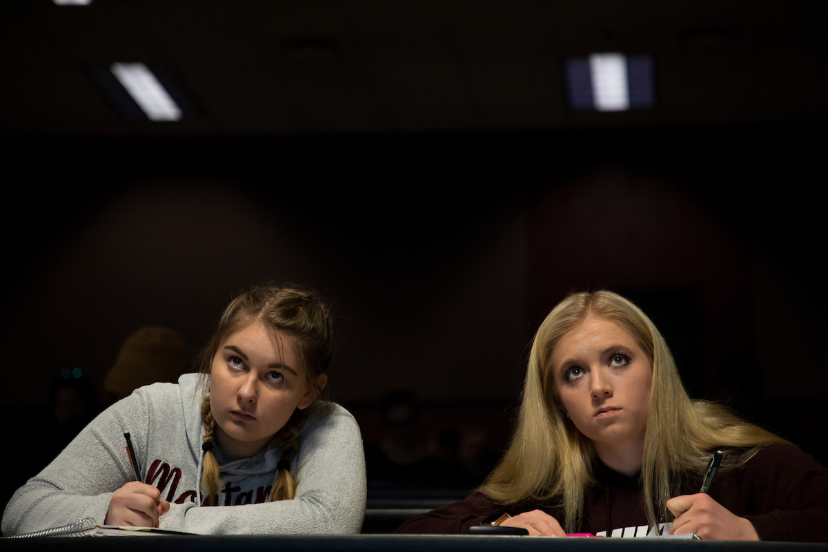 Two students looking up and taking notes
