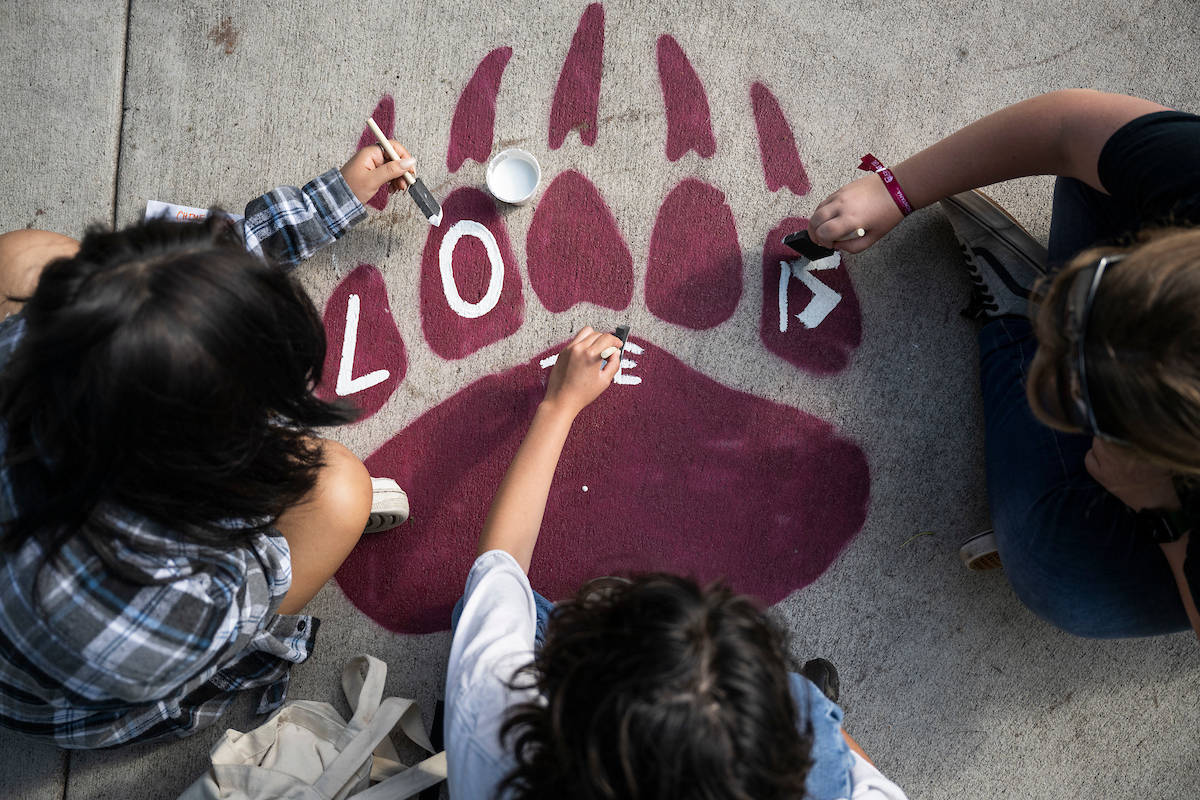 People painting the word “LOVE” on a large maroon paw print on a sidewalk.