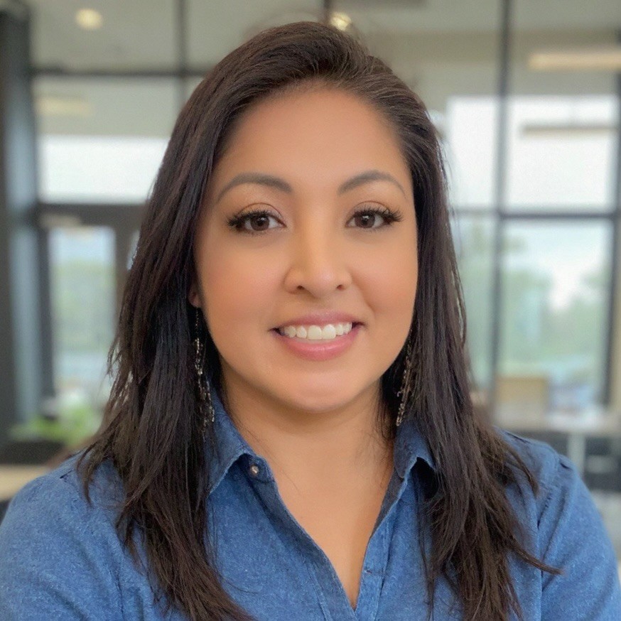 Professional portrait of a woman with long dark hair, smiling warmly against a blurred office background.