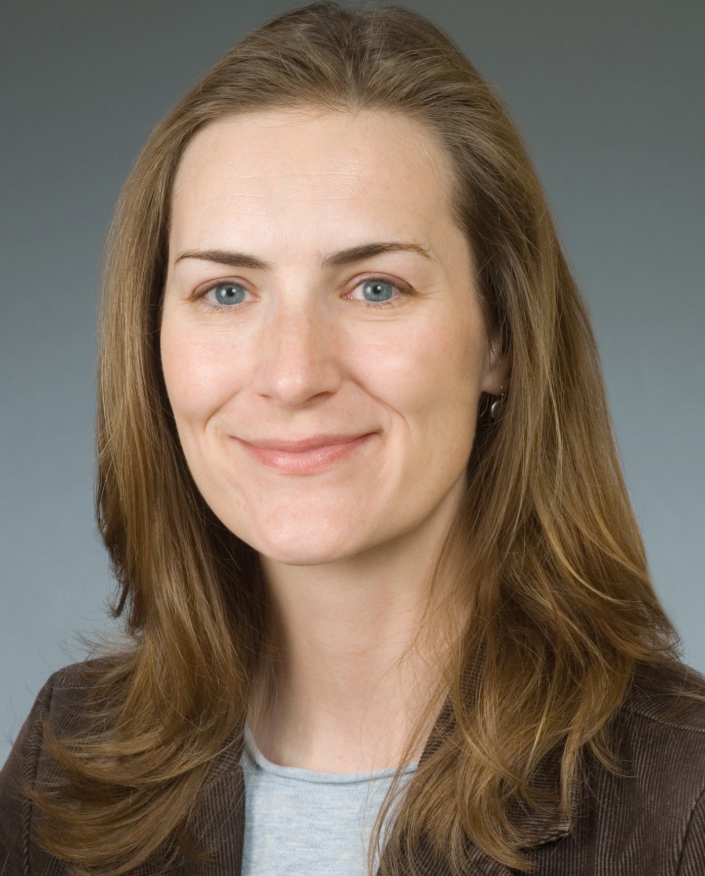 Professional headshot of a woman with medium-length brown hair, smiling and wearing a blazer.