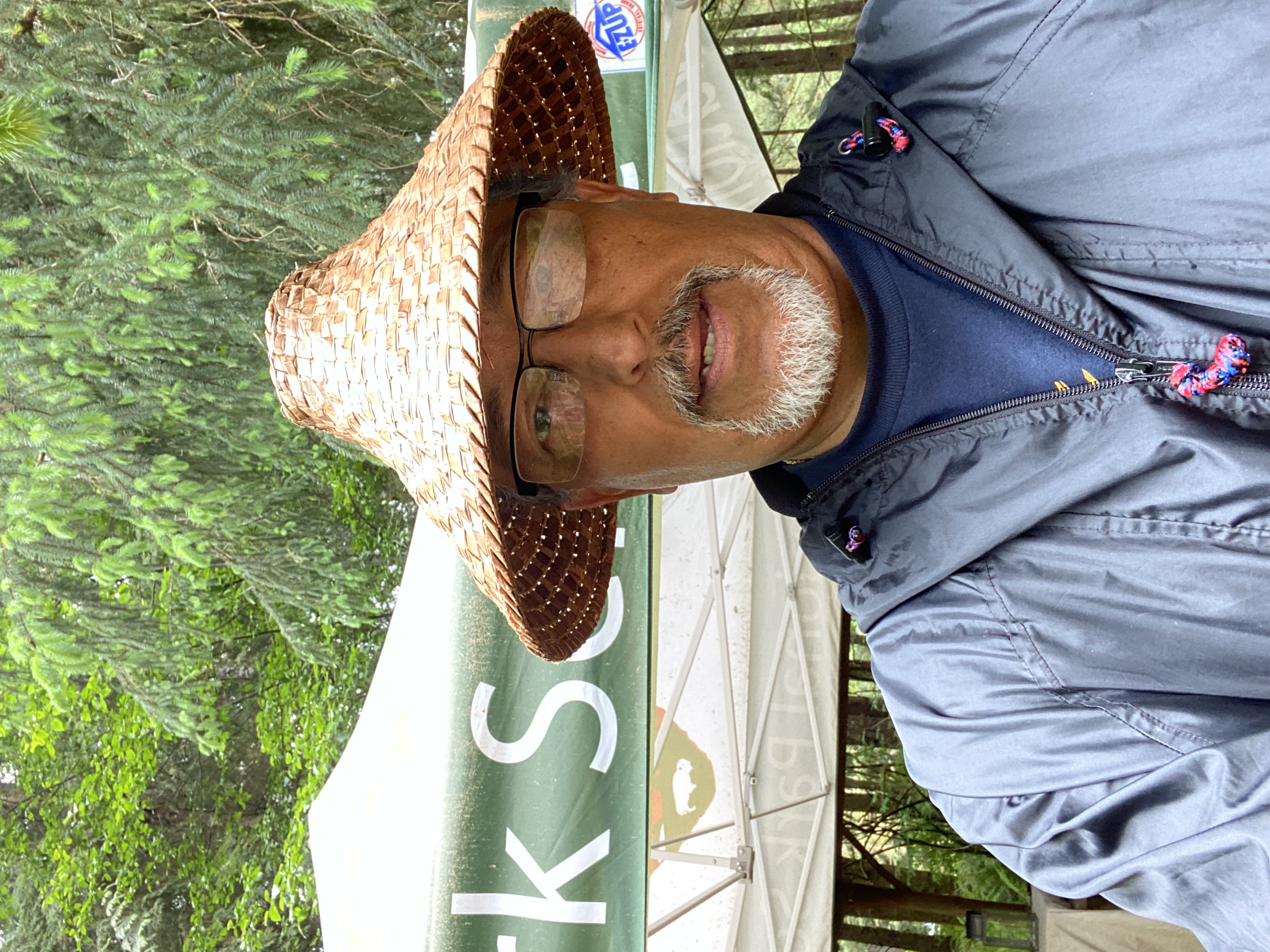 A man wearing a woven straw hat stands in front of a green tent labeled "Park School" surrounded by trees.