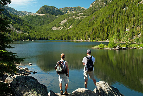 Two people stand with their backs to the camera looking at an alpine lake