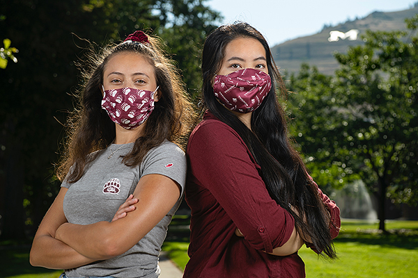 Two students wearing masks with M in background