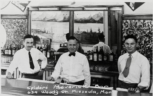 An old image of three men in white shirts and ties behind a bar counter. On the phot is written Spider's Maverick Bar 634 Woody St. Missoula, Mont