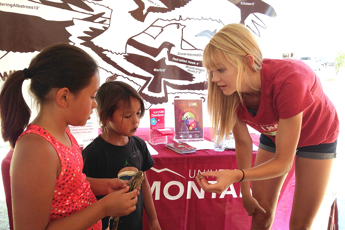 A spectrUM educator shares wildlife specimens with young visitors to the Science Learning Tent at the Arlee Celebration.