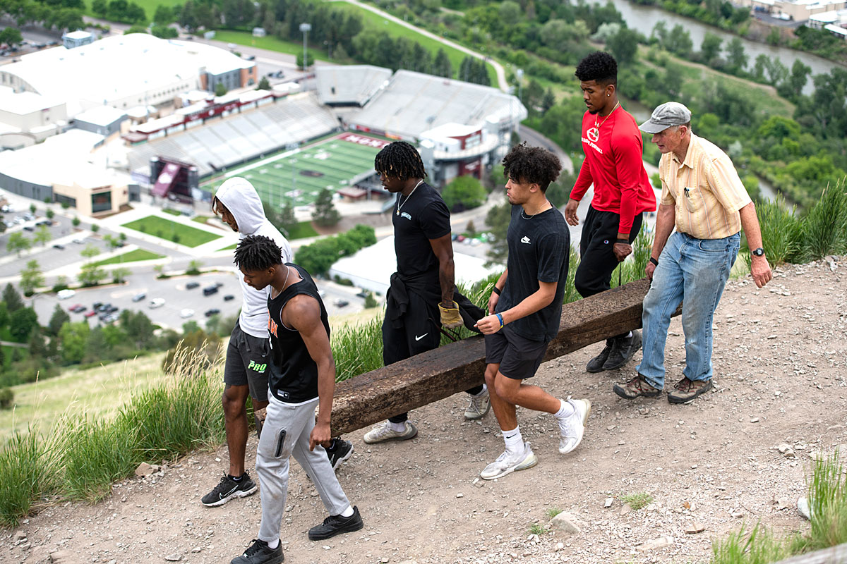 M Trail project leader Dr. Steve Gaskill carries a railroad tie with Griz football players earlier this summer.