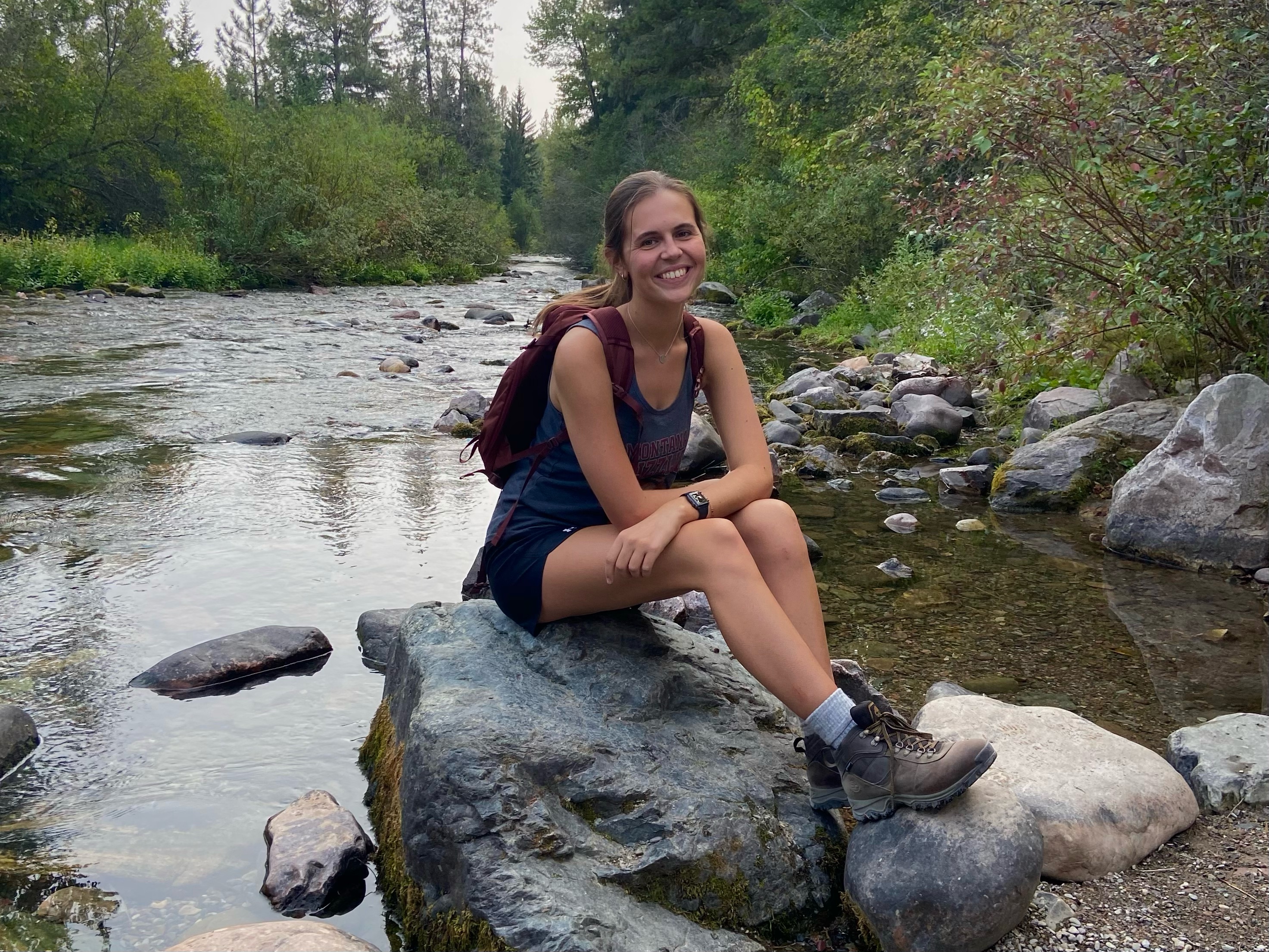 A UM student sits in a creek on a rock 