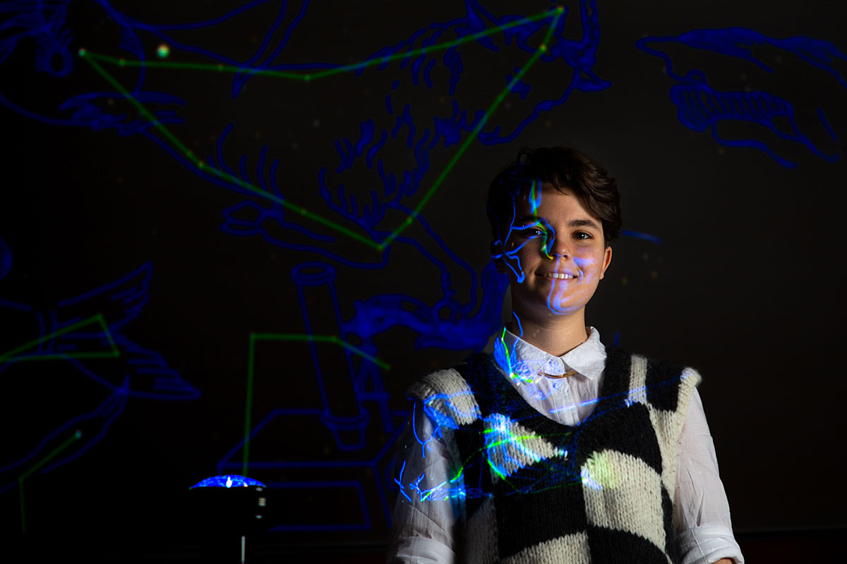 A picture of Ailey Robinson illuminated by projected light in the planetarium of UM's Payne Family Native American Center.