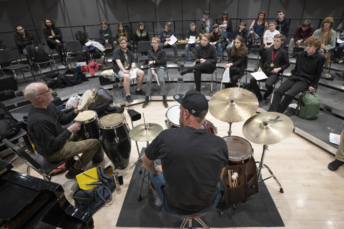 Wicks sits in front of a drum set in a classroom. 