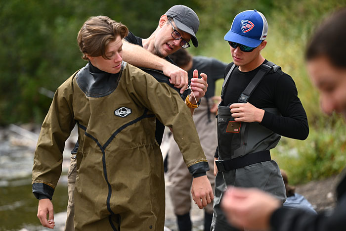 UM Associate Professor Andrew Whiteley helps student Teal Eisendrath don a dry suit as part of the Fisheries Techniques class. Student Eben Mayer can be seen in waders. 
