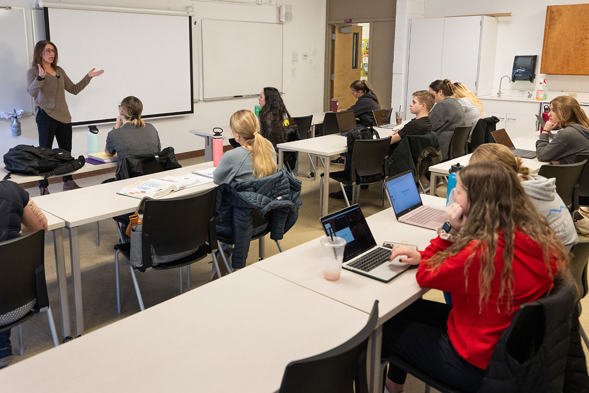 A teacher gestures in front of a class of students.
