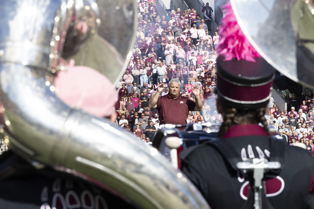 An image of Marching Band Director Dr. Kevin Griggs guiding the band through the national anthem on the football field. 