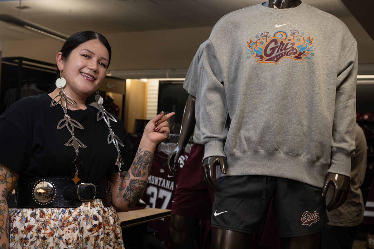 A photo of Kaylene Big Knife pointing at her Native Griz design. 