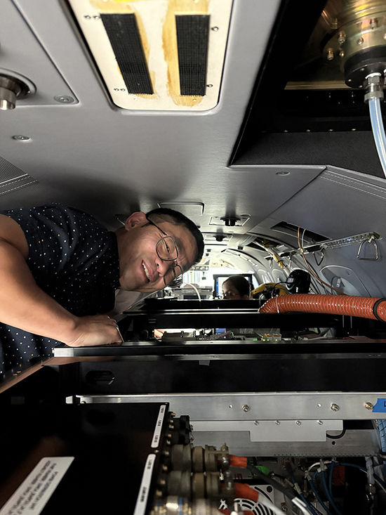 Lu Hu squeezes above equipment inside a cramped airplane.