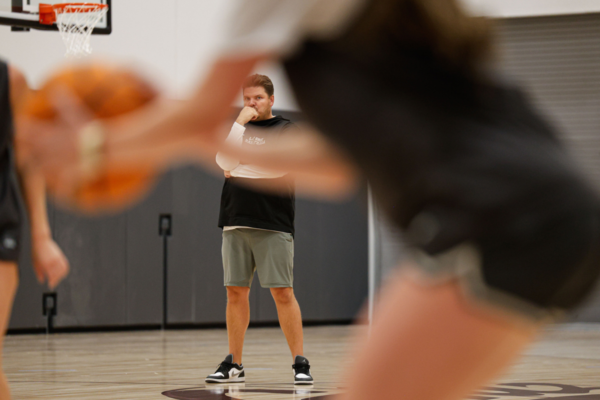 An image of Coach Hasrris watching his players run a drill at basketball practice. 