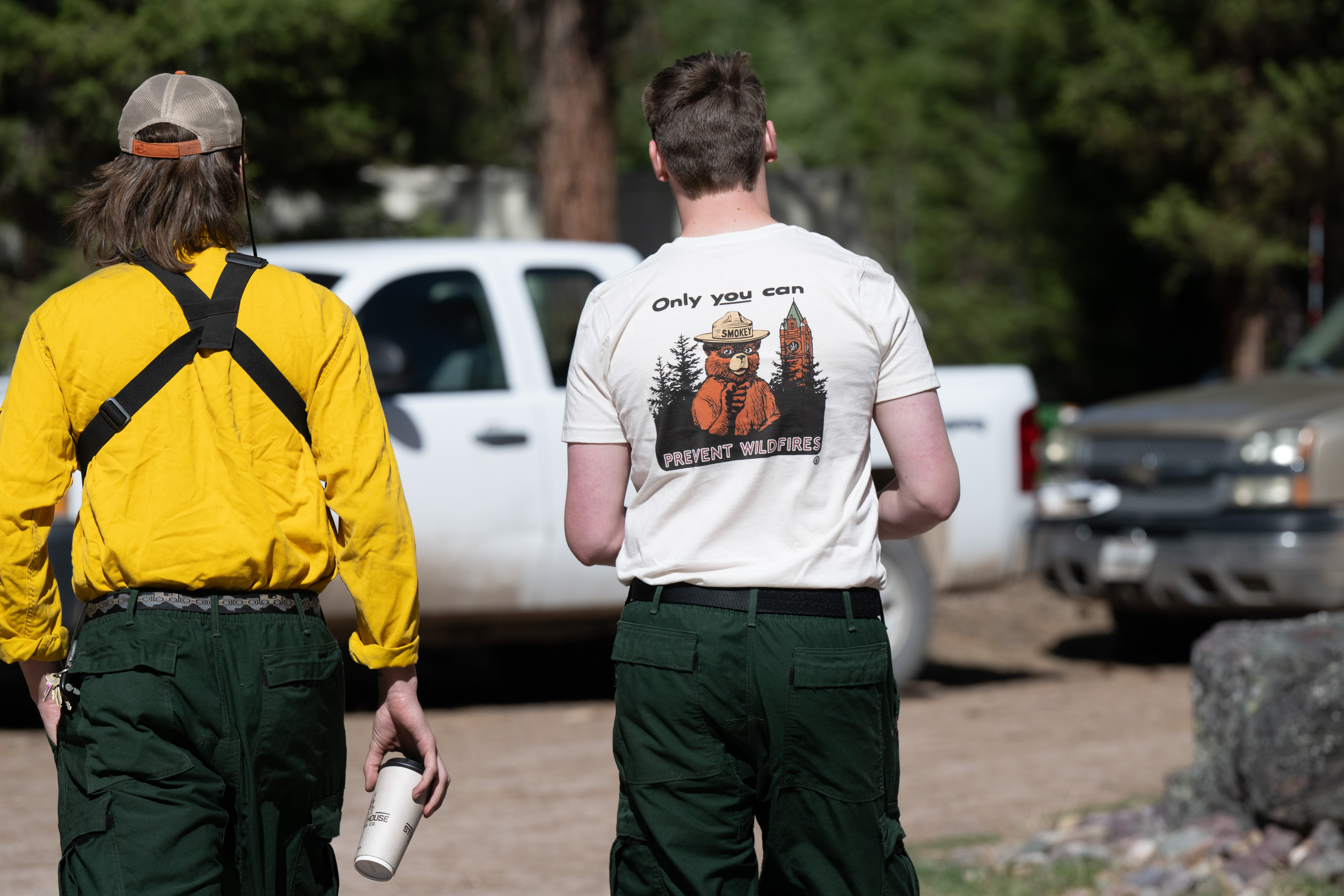 A UM student wears a Smokey Bear t-shirt while walking near a forest.