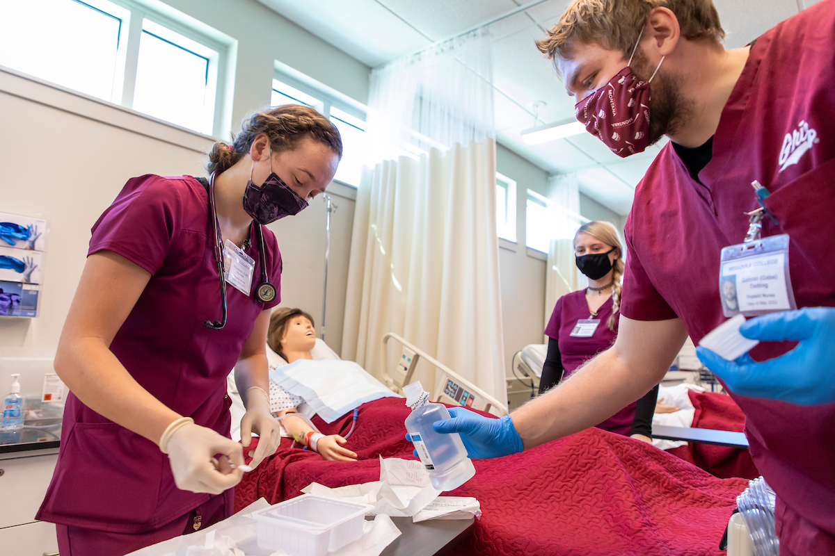 Three nursing students gather around a medial manikin