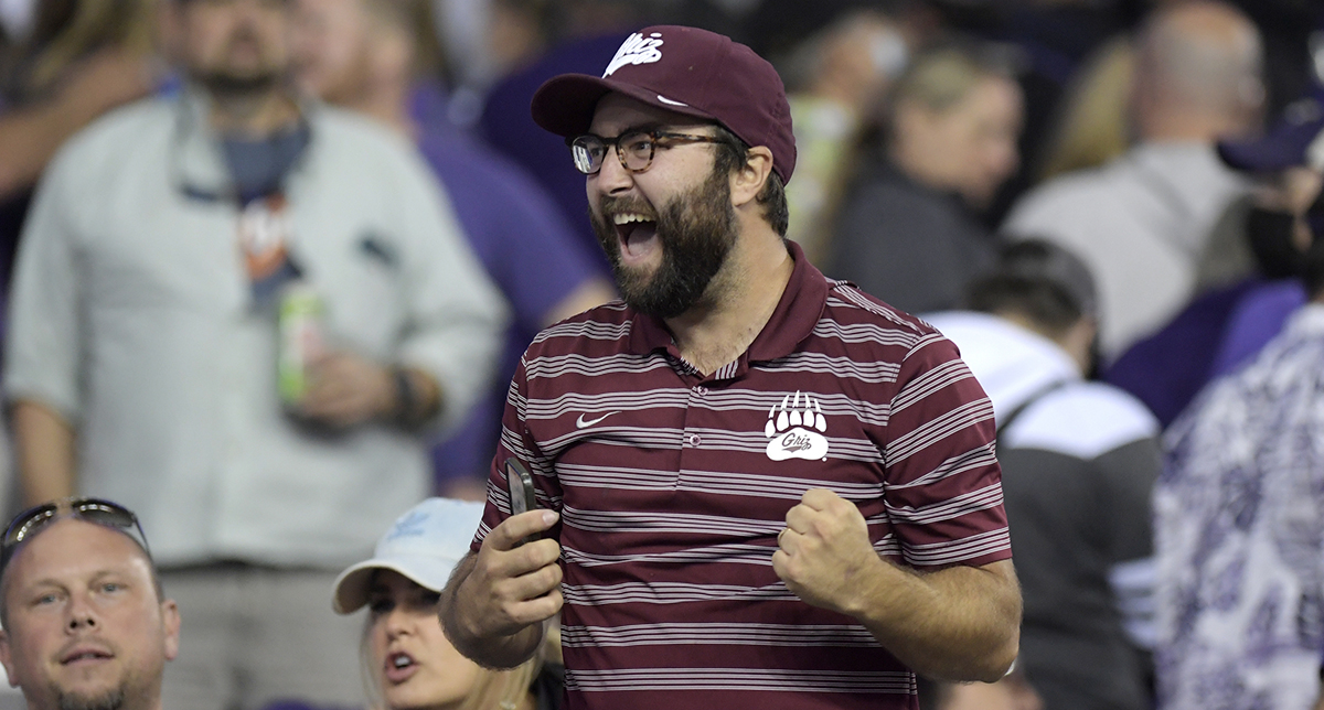 A man wearing a Griz hat cheering in a crowd at a football game