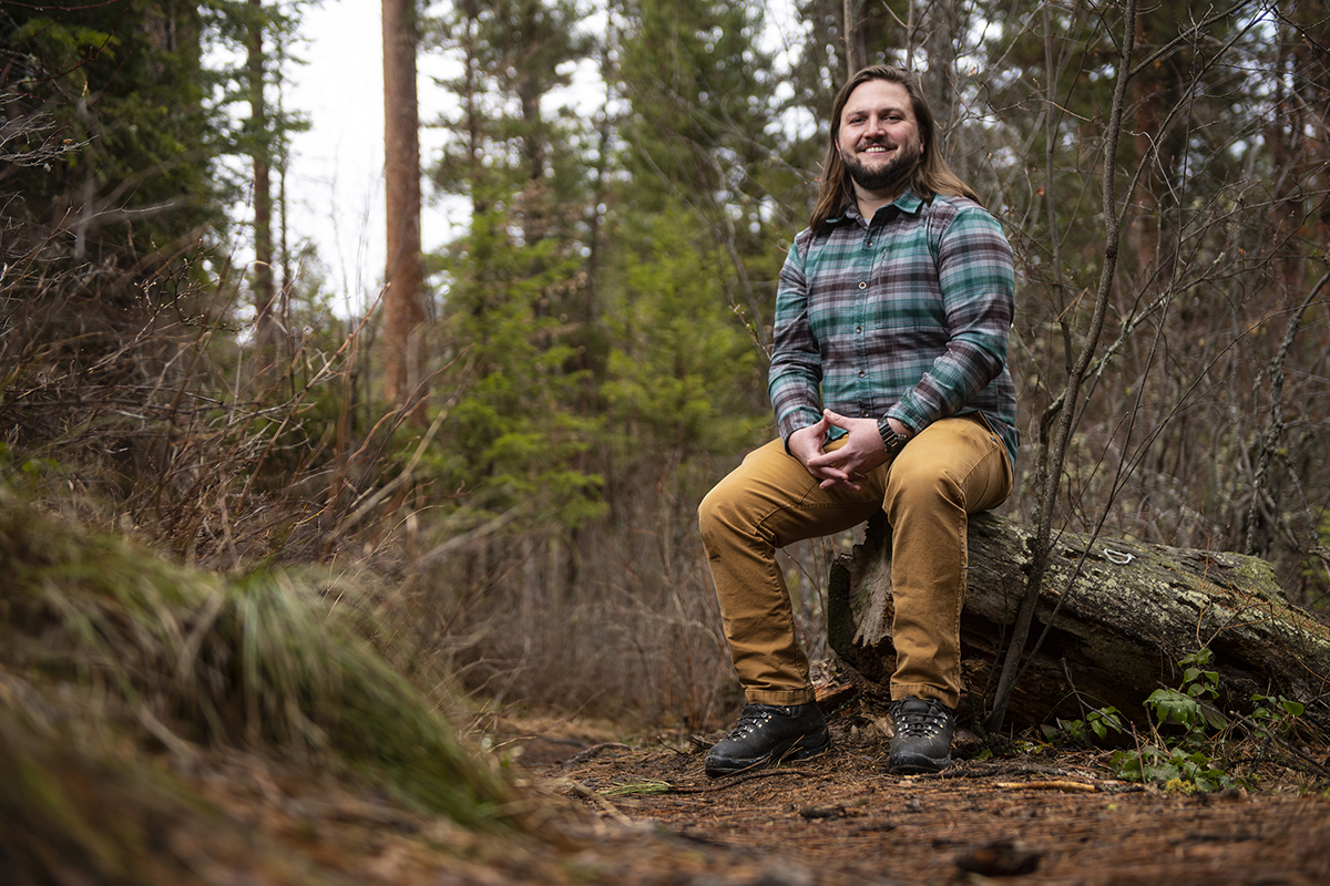 A UM student sits on a stump in the woods.
