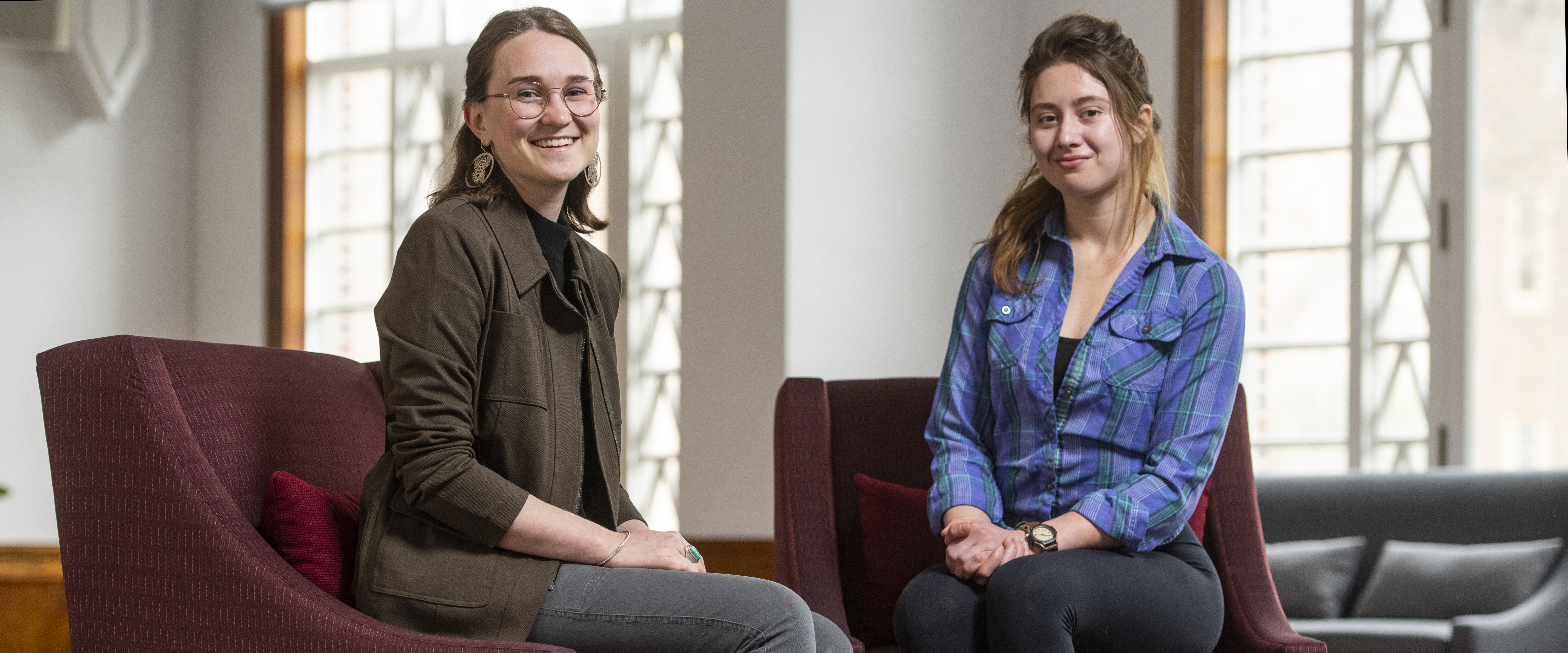 Two women sit in chairs in front of a window 